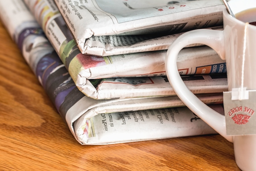 Three newspapers stacked next to each other next to a mug of tea.